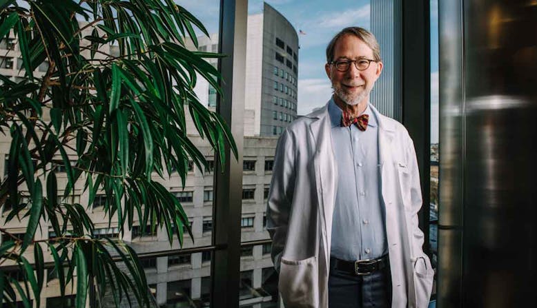 Doctor Philip Mease poses and smiles while wearing a bow tie and lab coat. 