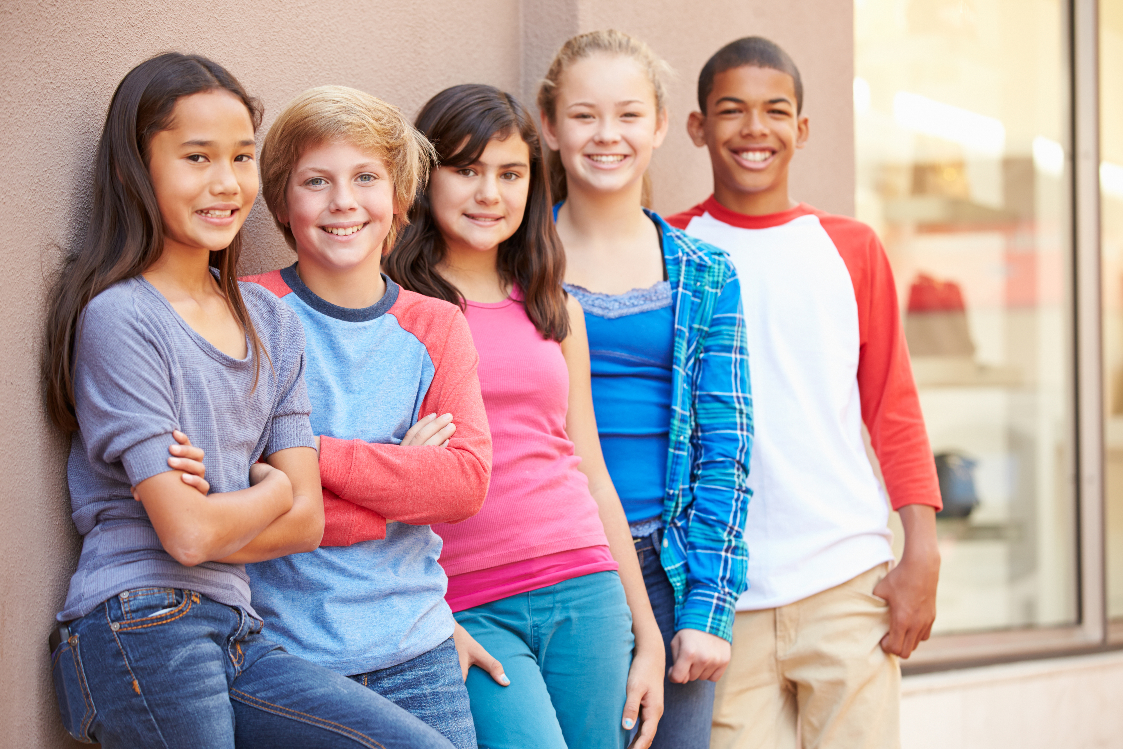 Group of kids stand together by a building smiling.
