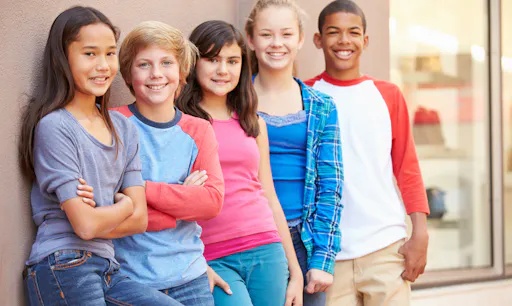 Group of kids stand together by a building smiling.