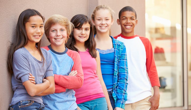 Group of kids stand together by a building smiling.