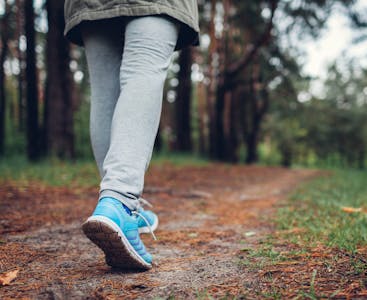A shot of a woman's legs as she is walking on a path through the woods.