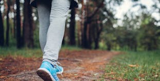 A shot of a woman's legs as she is walking on a path through the woods.