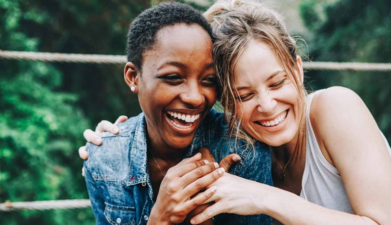 Two young women embrace and share a laugh.