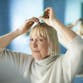 A woman looks in her bathroom mirror while applying treatment to her scalp.
