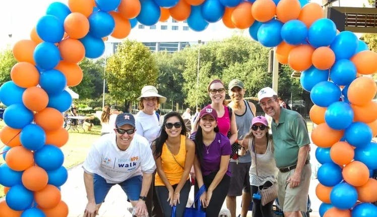 A group of people stand under an NPF balloon arch at an NPF event.