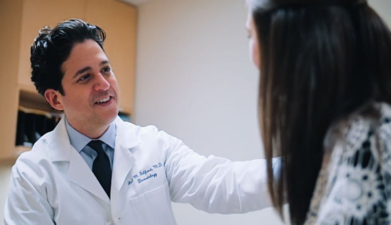 Male doctor talks to a female patient in an exam room.