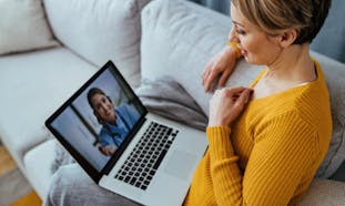 A woman sits with her laptop while asking a doctor a question over a video call.