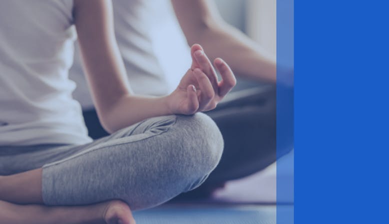 Two people sit and meditate while sitting on yoga mats.