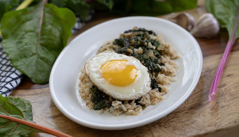 A dish of health grains and greens with a fried egg on top.