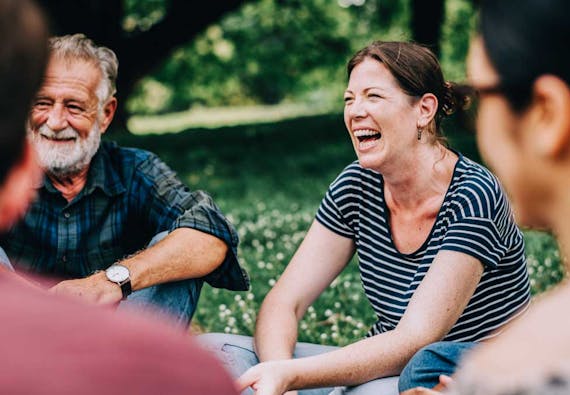 A woman sits outside with a group of others and laughs. 