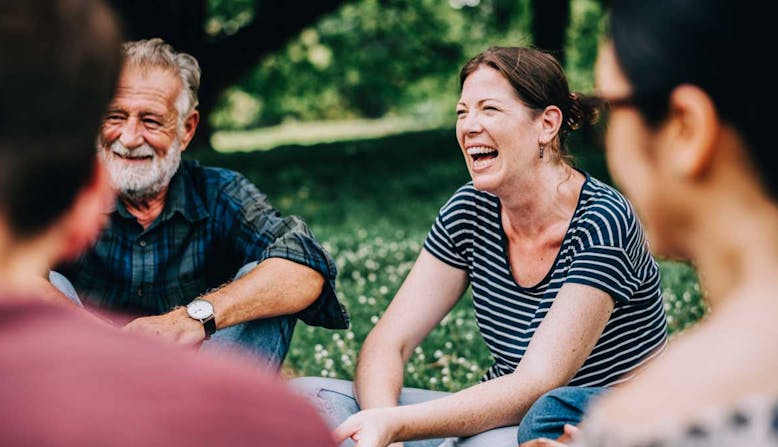 A woman sits outside with a group of others and laughs.