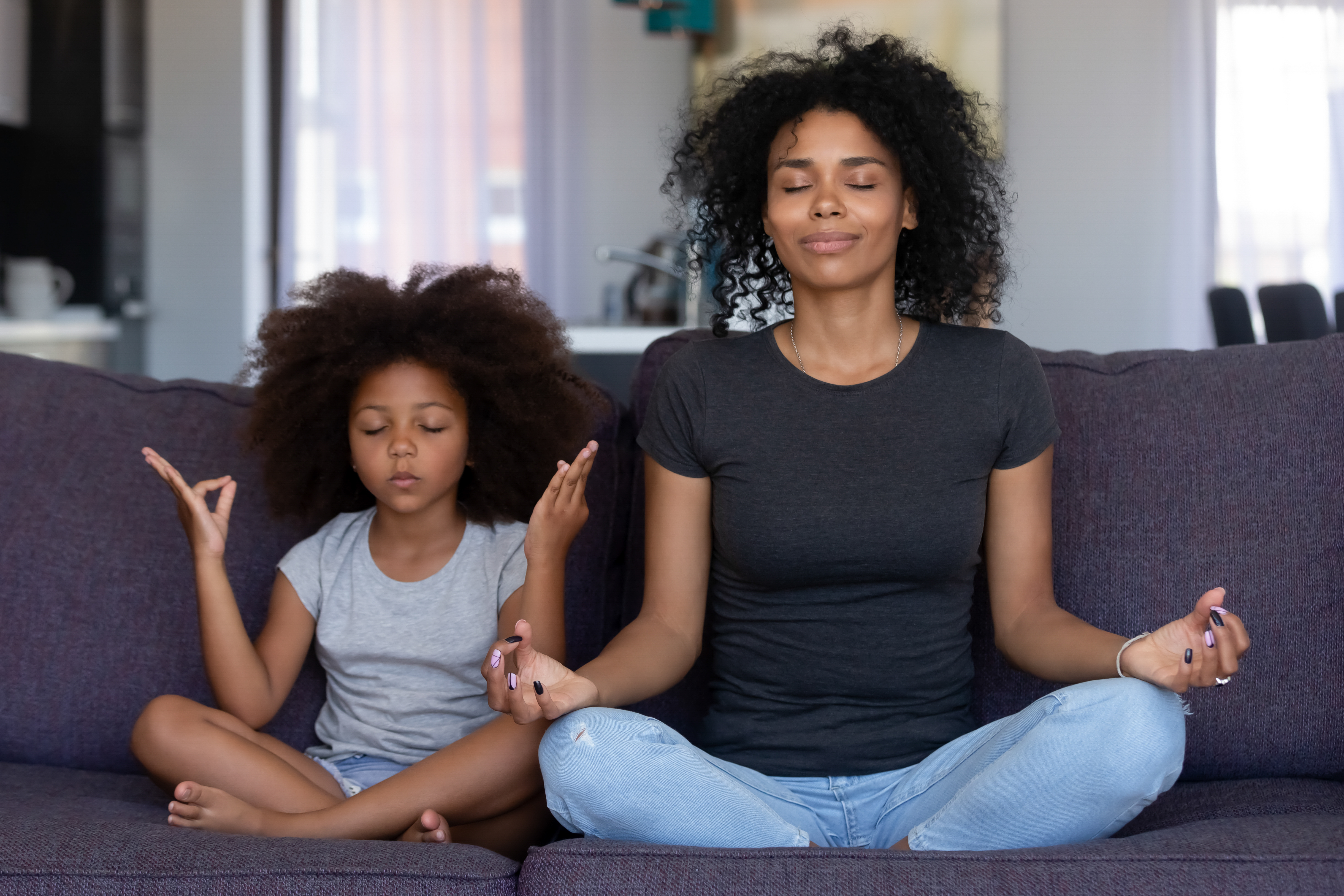 A mother sits on the couch with her daughter meditating.