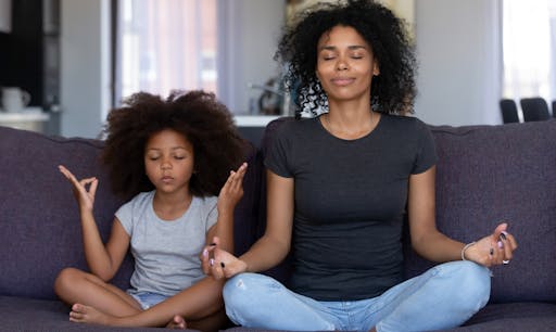 A mother sits on the couch with her daughter meditating.