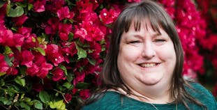Rachel English of Tucson, Arizona smiles in front of a wall of red flowers.