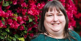 Rachel English of Tucson, Arizona smiles in front of a wall of red flowers. 