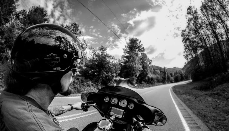A black and white photo of Kelby Caldwell on a motorcycle along a winding road.
