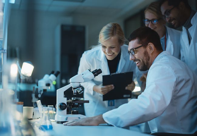 Happy male research scientist makes an important discovery while researching samples under the microscope.