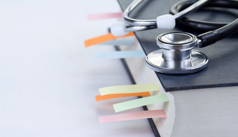 A textbook with flag notes sticking out with a stethoscope sitting on top.