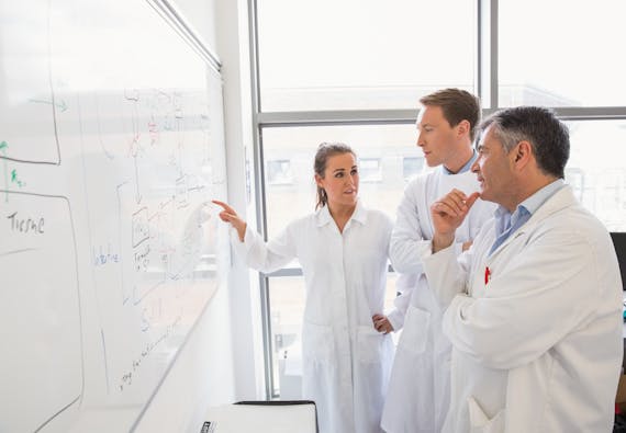 Three people in lab coats looking at a whiteboard