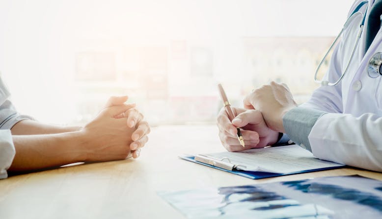 A doctor and patient seen from the neck down reviewing a medical chart.