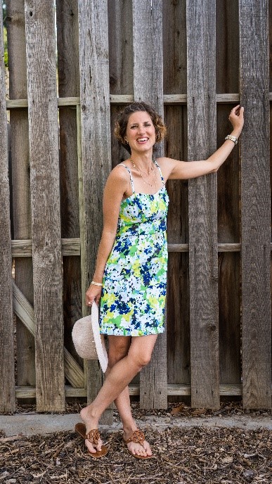 Sabrina Skiles smiling in a floral dress in front of a tall wooden fence.