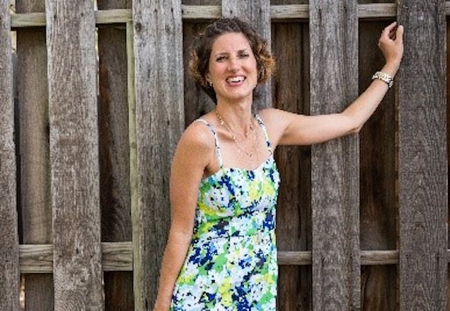 Sabrina Skiles smiling in a floral dress in front of a tall wooden fence.