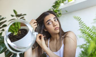 A nervous girl running her fingers through her hair and thinking about about dandruff and hair loss.