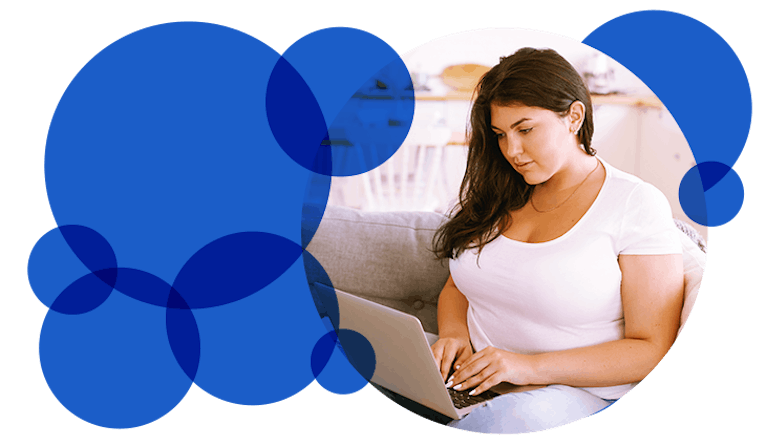 A woman is sitting on the couch and using a laptop.