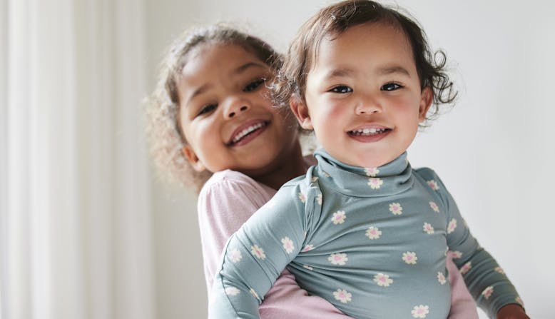 A young girl is holding a baby, both are smiling.