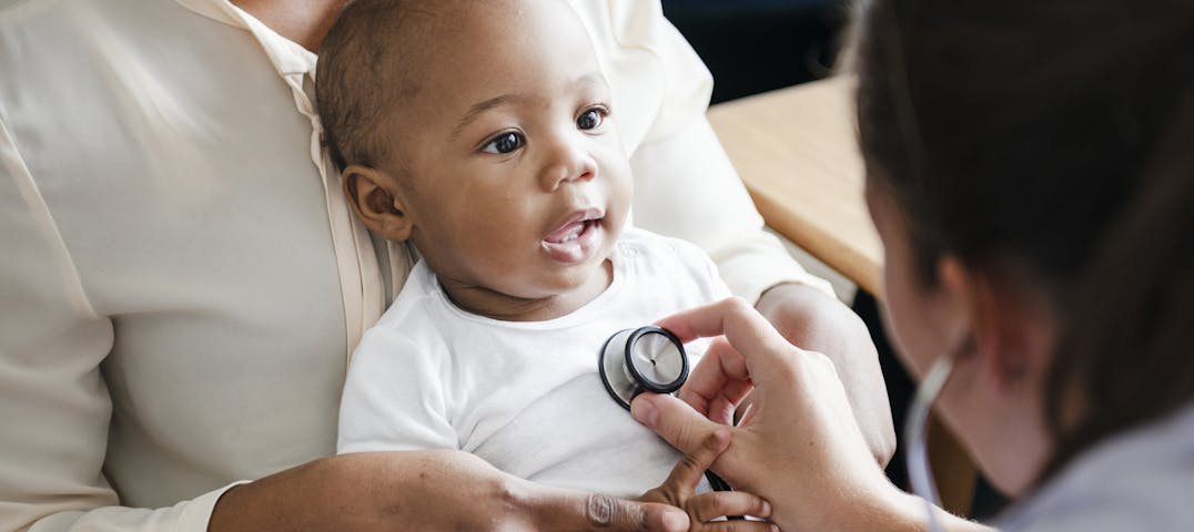 A doctor listens to the heart of an infant in the arms of a parent.