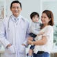 A doctor stands and smiles with a parent and her child in a clinic.