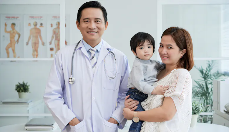 A doctor stands and smiles with a parent and her child in a clinic.