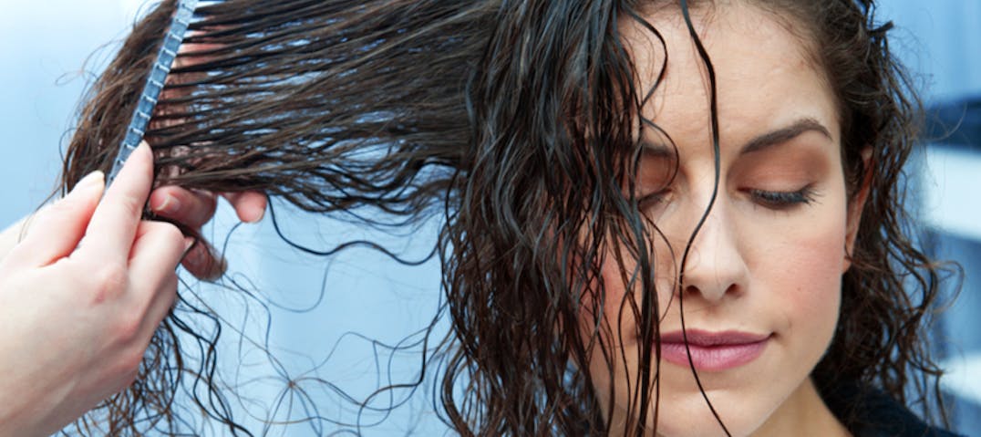 A woman has her hair combed by another.