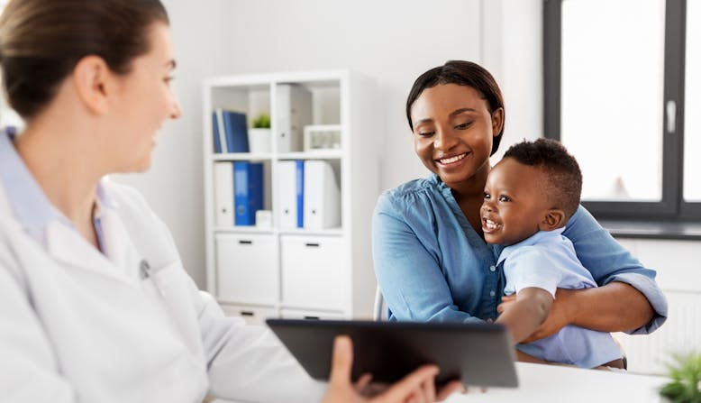 african american mother with baby son and caucasian doctor with tablet computer at clinic