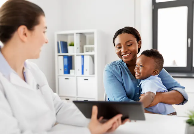 An African American mother with a baby son and a caucasian doctor with a tablet computer at the clinic.