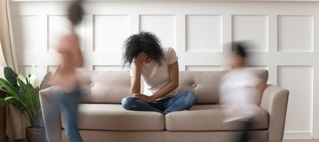 Two kids running in a living room, with a woman sitting on the couch exhausted.