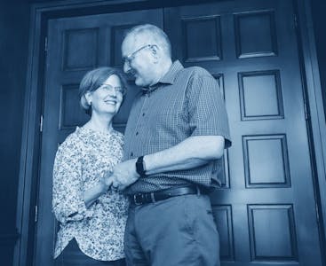 Nancy and Don Alpert smile and embrace each other in front of a door.