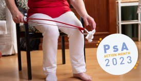 An elderly woman using a reacher tool to pick up a sock. PsA Action Month 2023 graphic overlaid.