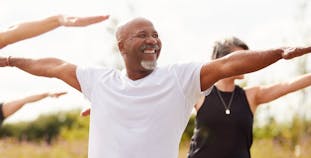 A man smiles while stretching outside with others. 