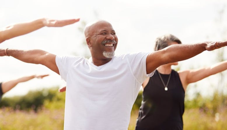 A man smiles while stretching outside with others.