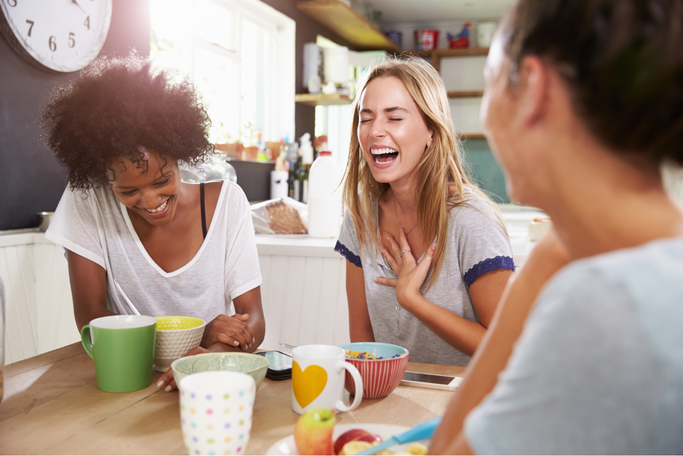 A group of women sit around a table drinking coffee and laughing. 