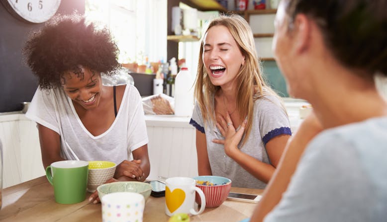A group of women sit around a table drinking coffee and laughing. 