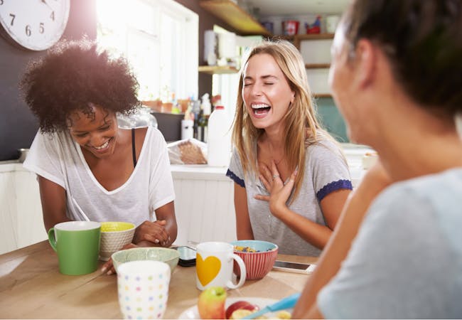 A group of women sit around a table drinking coffee and laughing. 