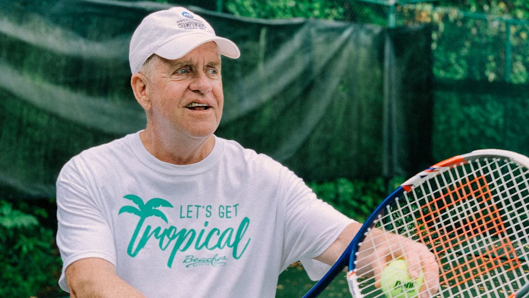 A man in a white hat playing tennis with psoriatic arthritis.