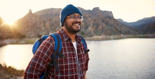 A young adult backpacker smiles at the lake view with a sunset behind him in the mountains.