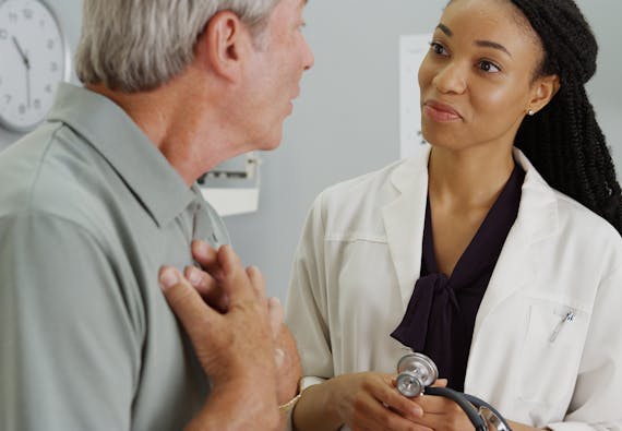 A female doctor listens as a patient speaks and holds his chest.
