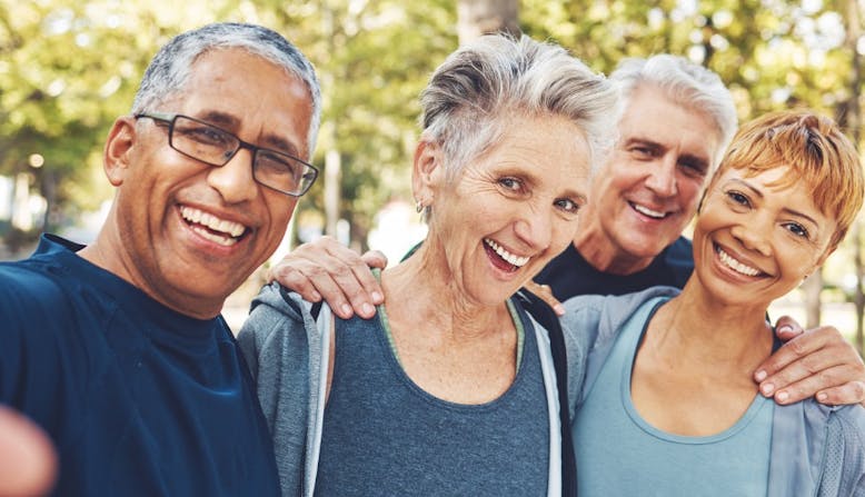 A multicultural group of elderly people smile outside.