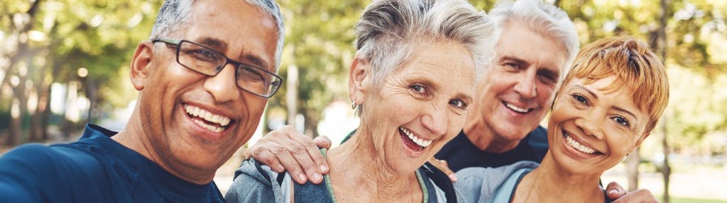 A multicultural group of elderly people smile outside.