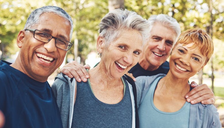 A multicultural group of elderly people smile outside.