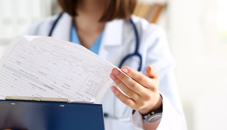 Female medicine doctor hand holding silver pen looking in clipboard pad closeup.